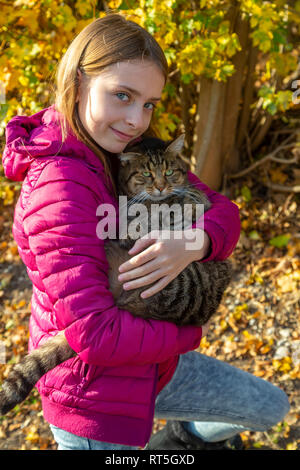 Portrait of smiling girl holding tabby cat outdoors in autumn Stock Photo