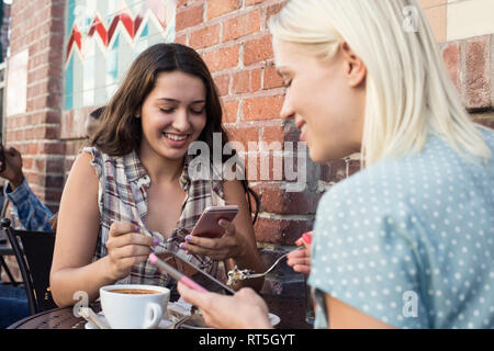 Two young women using cell phones at outdoor cafe Stock Photo