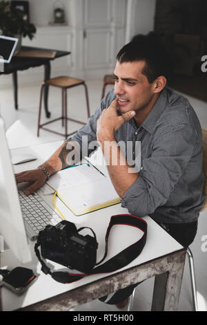 Young man with camera sitting at desk using computer Stock Photo