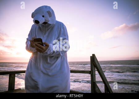 Denmark, Nordjuetland, Man wearing ice bear costume at the beach, using smartphone Stock Photo