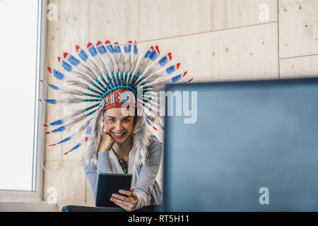 Young woman wearing Indian headdress, standing in office, using digital tablet Stock Photo