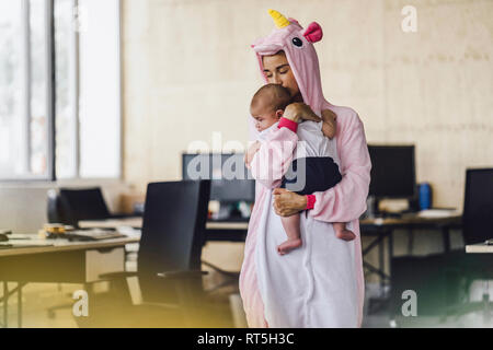 Young mother wearing unicorn onesie, standing in office, holding her