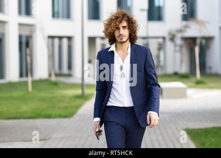 Portrait of young fashionable businessman with curly hair wearing blue suit Stock Photo