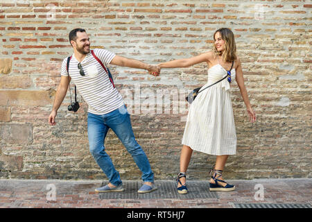 Happy couple holding hands walking in opposite directions at brick wall Stock Photo