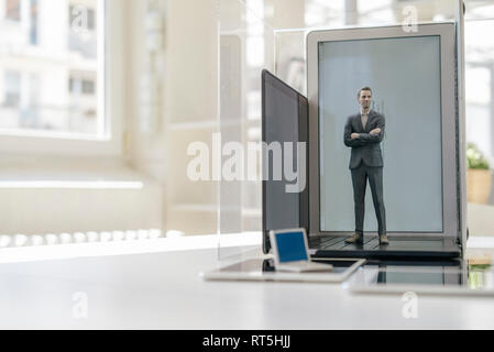 Businessman figurine standing on portable devices in a glass cage Stock Photo