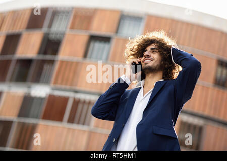 Portrait of young smiling fashionable businessman with curly hair on the phone Stock Photo