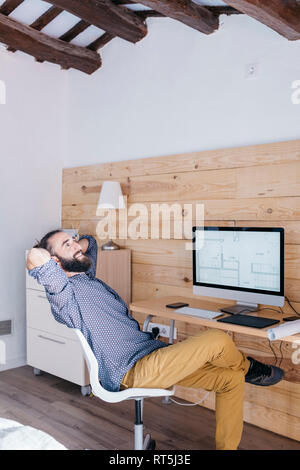 Smiling young man sitting at desk with floor plan on the computer Stock Photo