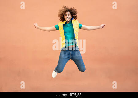 Portrait of smiling young man with curly hair wearing yellow waistcoat jumping in the air Stock Photo