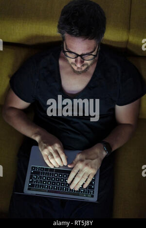 Man sitting on couch using laptop at night Stock Photo