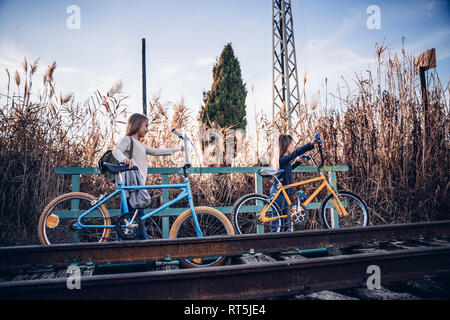 Two girls walking on the train track with bicycles