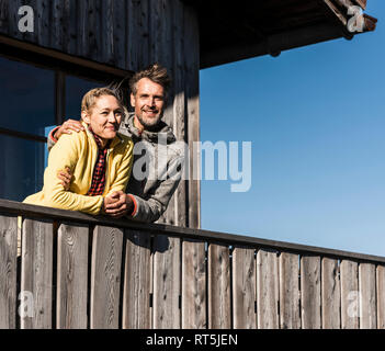Couple leaning on balcony of a mountain hut, with arms around Stock Photo