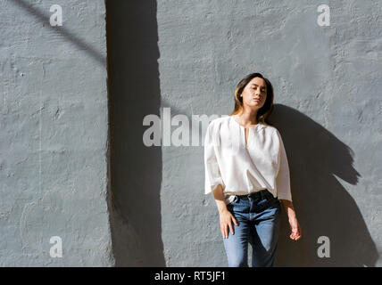 Portrait of young woman leaning against grey wall Stock Photo