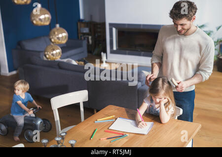 Father brushing daughter's hair, while she is drawing Stock Photo