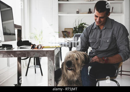 Young man sitting at desk stroking dog Stock Photo