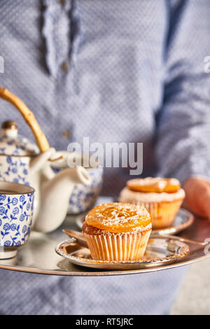 Woman serving fresh muffins and tea on silver platter, close-up Stock Photo
