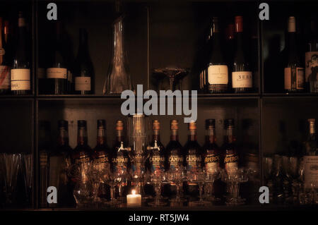 Several cocktail glasses and bottles of wine, Campari and Aperol on the shelves behind a bar. Stock Photo