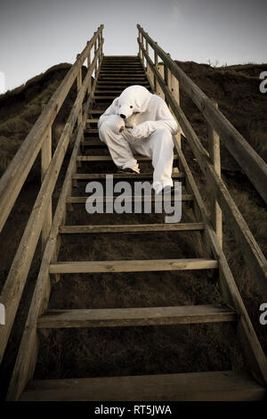 Man wearing ice bear costume sitting on steps, despair Stock Photo