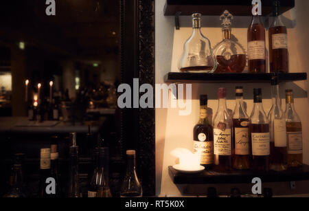 A large mirror and several bottles of alcohol on the shelves behind a bar. Stock Photo