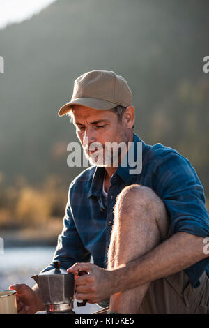 Mature man camping at riverside, using espresso machine Stock Photo