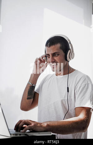 Smiling young man wearing headphones and using laptop Stock Photo