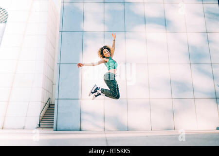 Portrait of happy young woman jumping at a building