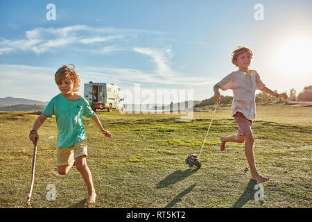 Chile, Talca, Rio Maule, two boys running on meadow with toy cars beside camper Stock Photo