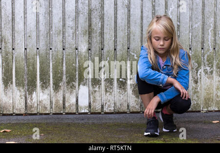 Portrait of serious blond girl crouching in front of wooden wall Stock Photo