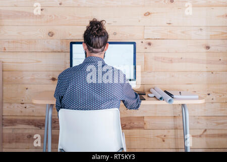 Rear view of young man working on floor plan at home using the computer Stock Photo