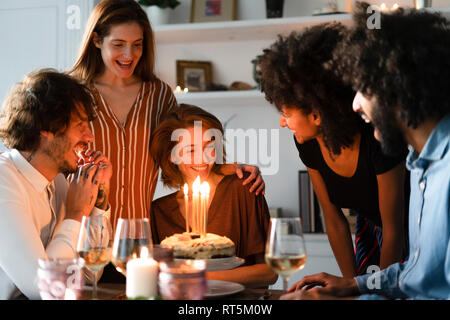 Friends surprising young woman with a birthday cake with burning candles Stock Photo