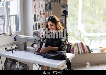 Smiling young fashion designer using sewing machine in her atelier Stock Photo