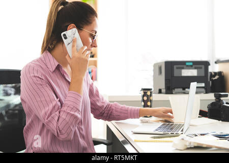 Designer working in office, using laptop, talking on the phone Stock Photo