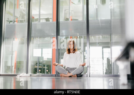 Businesswoman practicing yoga in office, meditating Stock Photo