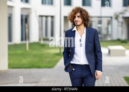 Portrait of young fashionable businessman with curly hair wearing blue suit Stock Photo