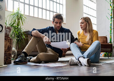 Businessman and businesswoman sitting on the floor discussing documents in loft office Stock Photo