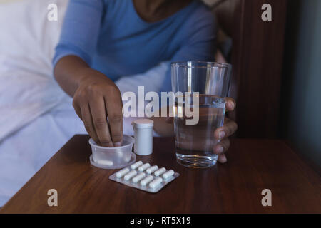 Senior woman taking medicine with glass of water in bed at home Stock Photo