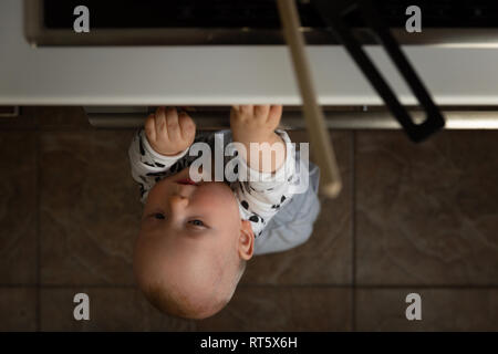 Little child playing with electric stove in the kitchen while sitting in highchair. Baby safety in kitchen Stock Photo