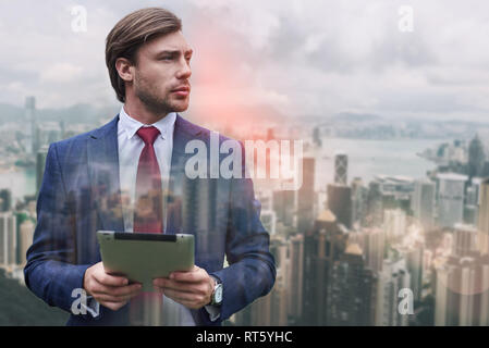 Ready to work. Stylish bearded businessman holding his digital tablet while standing against of cityscape background. Digital. Internet. Communication Stock Photo