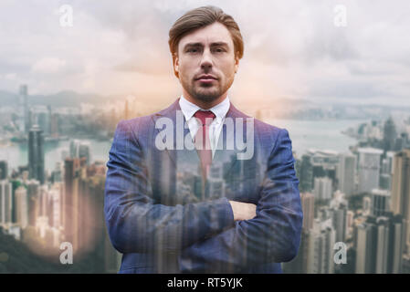 Everything should be perfect! Close-up portrait of handsome businessman keeping his arms crossed while standing against of cityscape background. Business concept. Success. Stock Photo