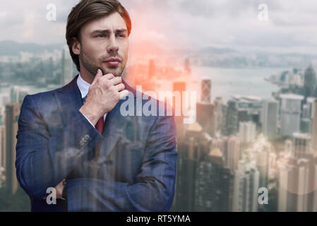 Thinking about business. Handsome bearded businessman touching his chin and looking away while standing against of cityscape background. Future. Business ideas Stock Photo