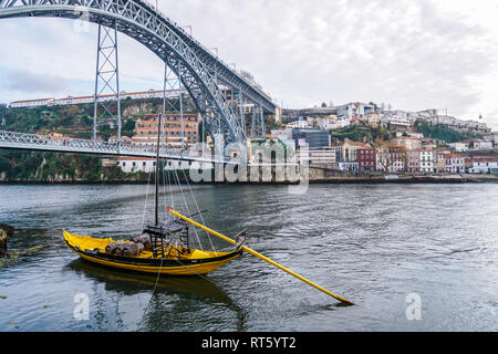 Porto, Portugal - December 2018: Yellow Rabelo Boat transporting port wine, in Douro River with Luis I Bridge behind. Stock Photo