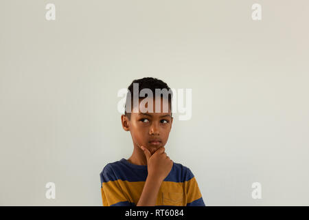 Boy with hand on chin standing against white background Stock Photo