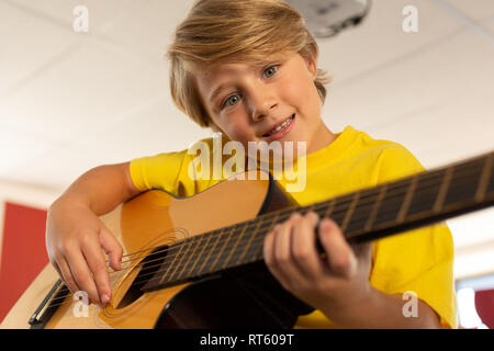 Boy looking at camera while playing guitar in a classroom Stock Photo