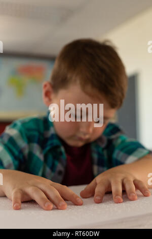 Blind boy reading a braille book at desk in classroom Stock Photo