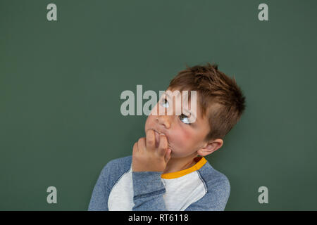 Thoughtful schoolboy standing against green chalkboard in a classroom Stock Photo