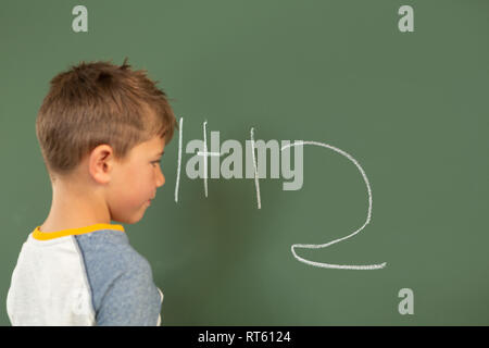 Schoolboy doing math on green chalkboard in a classroom Stock Photo