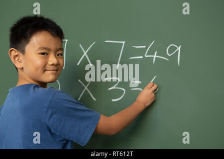 Schoolboy doing math on greenboard in a classroom Stock Photo