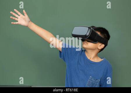 Schoolboy using virtual reality headset against greenboard in a classroom Stock Photo