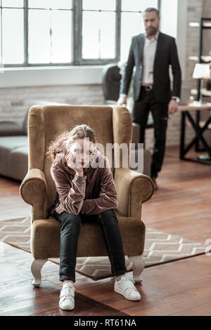 Sitting in armchair. Curly stylish teenager with dark makeup sitting in comfortable armchair Stock Photo