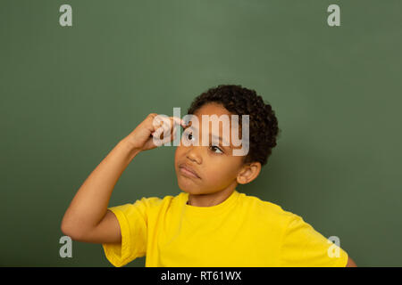 Thoughtful schoolboy with finger pointing to head standing against greenboard Stock Photo