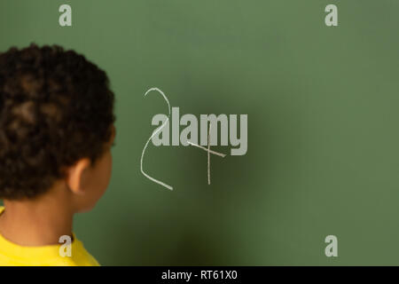 Schoolboy doing math on greenboard in a classroom Stock Photo